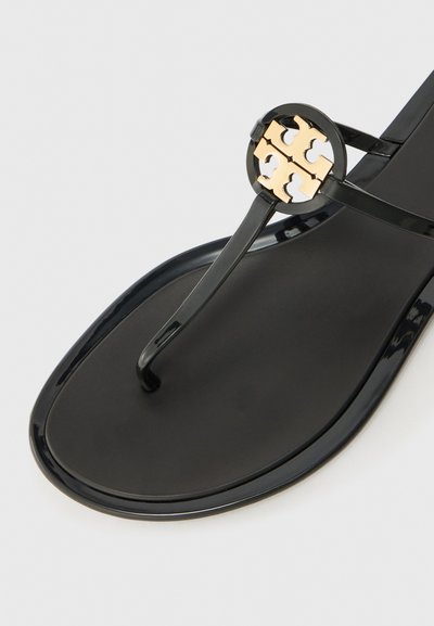 Svart flip-flop sandal med glansfull overflate, med en sirkulær gullakcent og et stilrent design. Teksturert såle for godt grep.