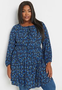 Sininen kukkakuosiset tunikamekko pitkillä hihoilla, elastisella vyötäröllä ja rypytetyllä kaula-aukolla. Mekossa on pieniä sinisiä ja vihreitä kukkia tummansinisellä taustalla.