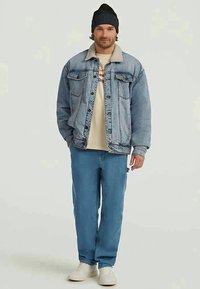 Ljusblå denimjacka med en beige fleecekrage, tillsammans med ljusblå kordbyxor och vita sneakers. Modellen bär en svartrandig mössa.