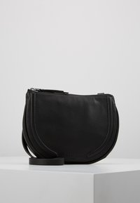 Borsa a tracolla nera in pelle con forma arrotondata, finitura texturizzata, chiusura con zip superiore e una tracolla removibile. Presenta un branding discreto.