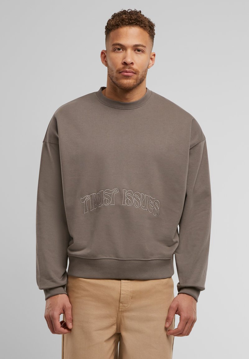 Szary sweatshirt o luźnym kroju, okrągłym dekolcie i żebrowanych mankietach, z haftowanym w kontrastowym kolorze napisem "Zaufanie w kryzysie".
