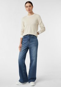 Gestreifter creme- und beigen Pullover mit langen Ärmeln, kombiniert mit hochtaillierten, dunkelblauen weiten Jeans und weißen Sneakers.