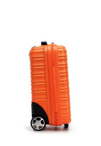 Valigia rigida arancione con texture a righe, pannello inferiore nero, maniglie laterali e base a quattro ruote per la mobilità.
