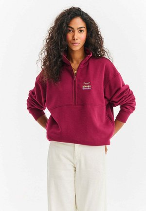 Bluza bordowa na zamek z wysokim kołnierzem i haftowanym logo "Naoko Studio". Miękki materiał, luźny krój i ściągacze na rękawach.