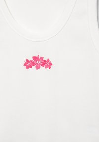 Haut blanc sans manches avec un petit groupe de trois fleurs d'hibiscus roses brodées centré près de l'encolure.