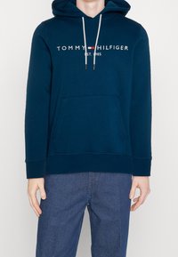 Felpa con cappuccio blu navy con tasca frontale, con cordoncini bianchi e logo "TOMMY HILFIGER EST. 1985" sul petto.