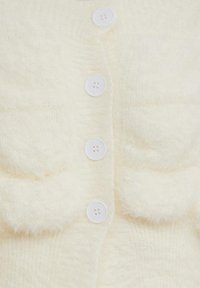 Mjukt krämfärgat cardigan med vertikal rad av vita knappar och två fluffiga framfickor, som framhäver stickad textur och mysigt tyg.