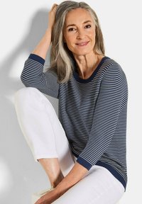 Marineblau-weißer gestreifter Langarmpullover mit geripptem Halsausschnitt und Bündchen, kombiniert mit weißen Hosen, die einen entspannten Schnitt und eine weiche Textur aufweisen.