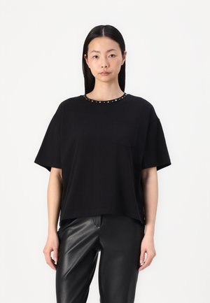 T-shirt à manches courtes noir avec un col rond orné de clous en argent et une petite poche sur la poitrine. Tissu en coton doux.