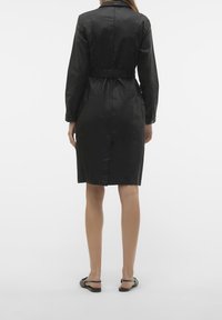Czarna sukienka z paskiem w talii, z długimi rękawami i prostym krojem. Gładki materiał z subtelnym połyskiem, sięgający tuż nad kolana. Prosty design.