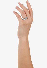 Anillo de banda de plata con múltiples acentos de piedras preciosas transparentes; acabado pulido y suave; exhibido en una mano con uñas de aspecto natural.