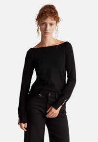 Černý svetr bez ramínek s ribbovaným výstřihem a dlouhými rukávy. Obsahuje boční rozparky v rukávech, spárovaný s černými kalhotami.