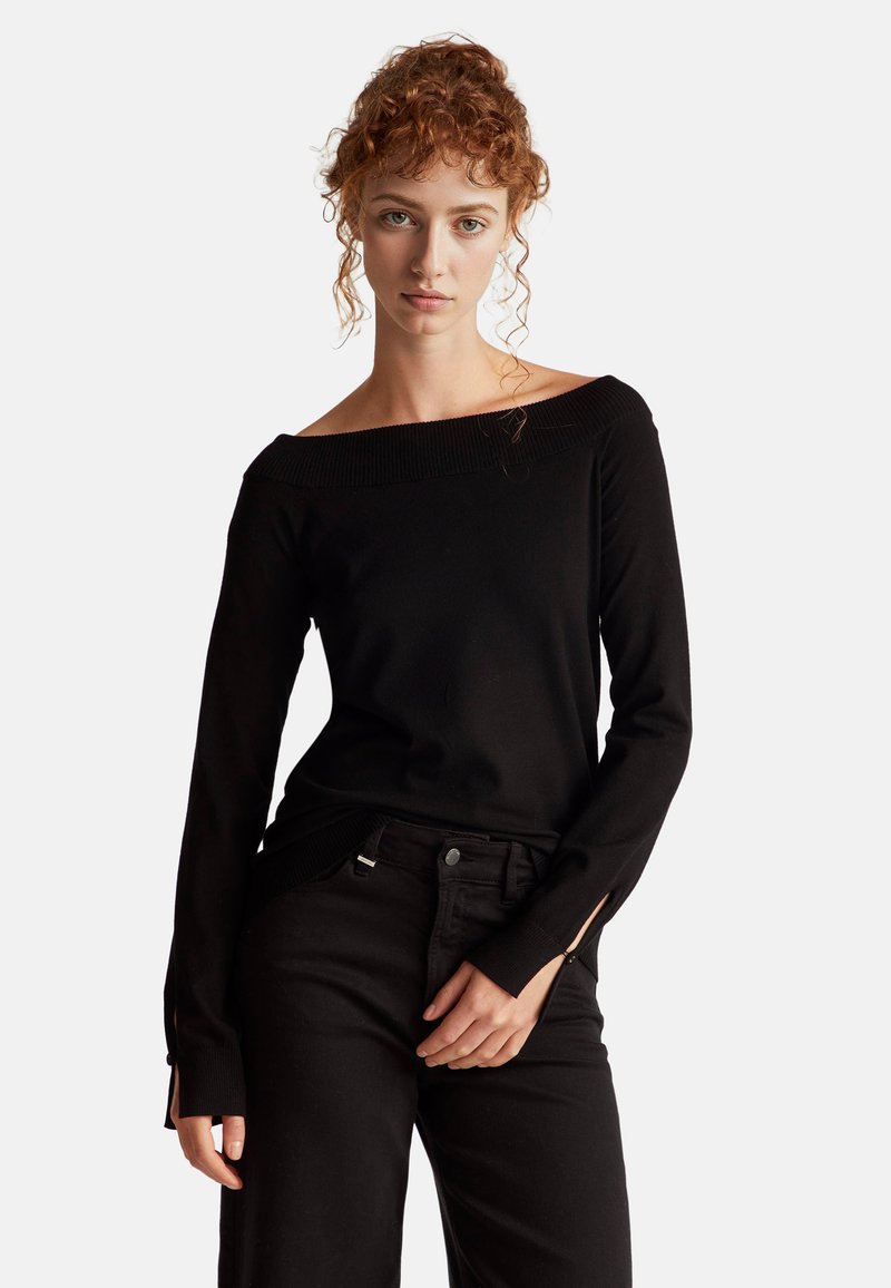 Černý svetr bez ramínek s ribbovaným výstřihem a dlouhými rukávy. Obsahuje boční rozparky v rukávech, spárovaný s černými kalhotami.