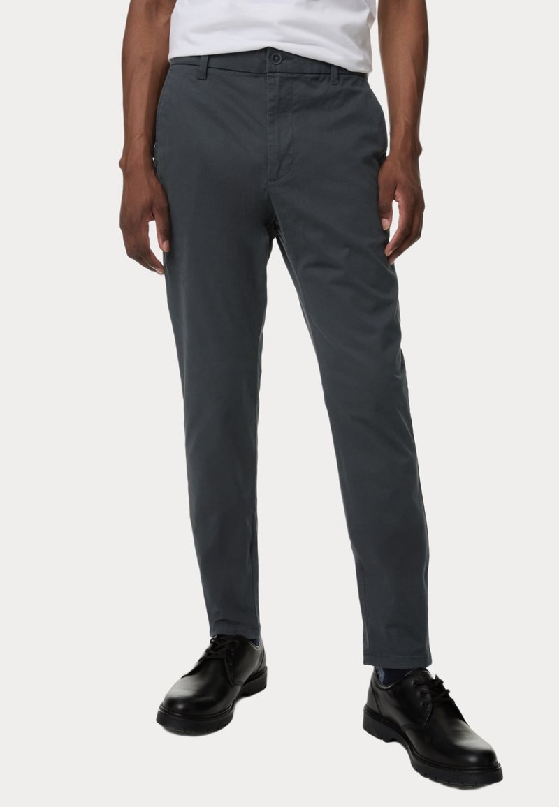 Grijze katoenen broek met een slim fit, voorzakken en een knoopsluiting. Draagt met zwarte schoenen, waardoor een gladde textuur zichtbaar is.