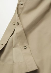 Tissu beige à texture lisse, avec de grandes pressions et des œillets en métal, bords cousus. Focus sur les détails et les éléments de design.