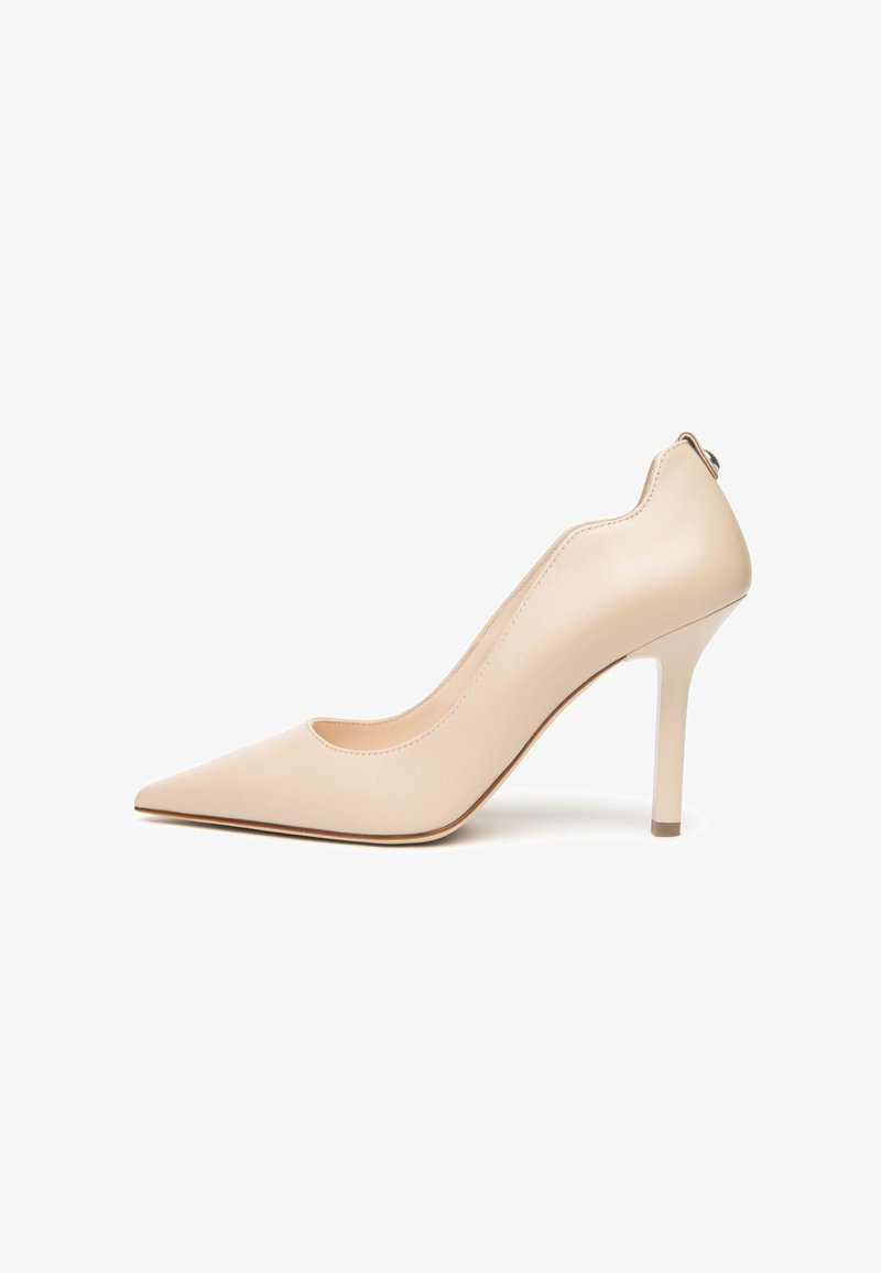 Escarpin beige à talon haut, bout pointu, bord festonné et talon aiguille fin, présenté sur fond blanc.