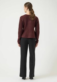 Maglione a coste bordeaux con maniche lunghe, scollatura rotonda e spacchi laterali, abbinato a pantaloni neri sartoriali e scarpe con tacco alto.