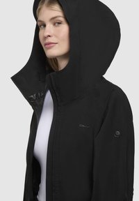 Black jacket with a large hood, zip front, and logo accents. Made from smooth fabric with a fitted design and visible stitching details.