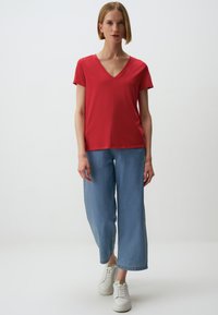 Rode V-hals T-shirt met korte mouwen, gecombineerd met lichtblauwe wijde jeans. Witte sneakers maken de casual outfit compleet. Soepele stoftextuur.