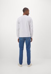 Witte blouse met lange mouwen en een ronde hals, gecombineerd met strakke blauwe jeans en lichtgekleurde sneakers; eenvoudig ontwerp, geen zichtbare patronen.