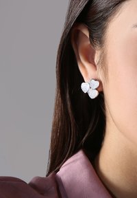 Silberne herzförmige Ohrringe mit drei verbundenen Elementen, die eine strukturierte Oberfläche und ein glänzendes Finish aufweisen. Geeignet für lässige oder formelle Anlässe.