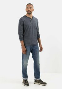 Grå langærmet Henley skjorte med en knaplukning ved halsen, parret med lyseblå jeans og mørkt fodtøj med grå og brune accenter.