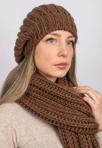 Hnědá pletená baret s texturovaným vzorem, nošený s odpovídajícím huňatým šálkem, obojí v bohaté, teplé barvě a měkké vlněné textuře.