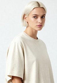 Beige kokvilnas T-krekls ar brīvu piegriezumu, apaļu kakla izgriezumu un nolaistām plecu šuvēm; gluda tekstūra un atturīgs dizains bez rakstiem.