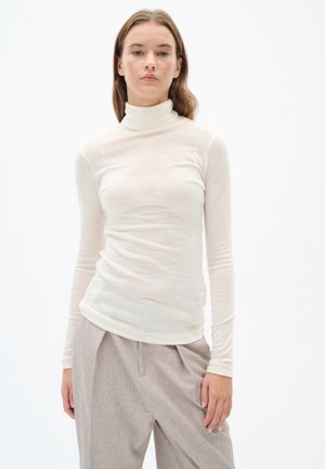 Langärmliges Turtleneck-Shirt in hellem Beige, aus weichem, transparentem Stoff. Mit einer figurbetonten Silhouette und einer glatten Textur, kombiniert mit hochtaillierten Hosen.
