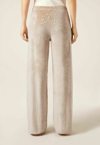 Široké kalhoty v světle béžové barvě, pokryté lesklými flitry, s hladkým povrchem a rovnou siluetou.