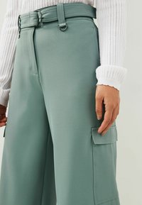 Välarmade cargo-byxor med vida ben i ljusgrön tyg med en slät textur, som har ett bälte, sidofickor och en skräddarsydd passform.