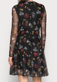 Robe noire à manches longues transparentes, ornée d'un imprimé ludique de motifs de dessins animés rouges, jaunes et argentés. Jupe évasée avec un buste ajusté.