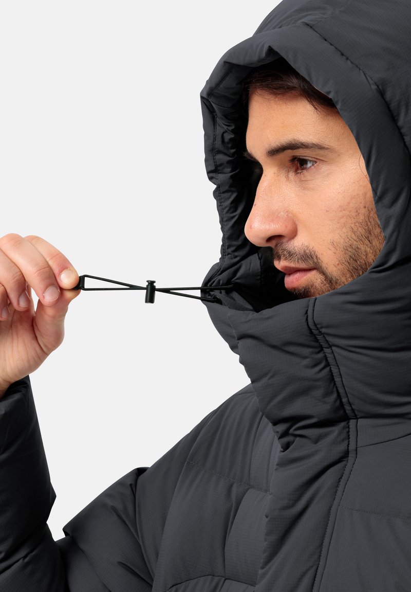 Schwarze Pufferjacke mit Kapuze, leichtes Material, gestepptes Muster, verstellbarer Kordelzug, Nahaufnahme einer Hand, die den Knebel greift.