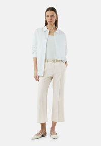 Witte overhemd met knopen over een witte tanktop, crèmekleurige wijde broek met zijdelingse piping en puntige flats met slingbackontwerp.