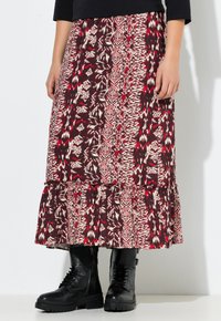Mujer que lleva una falda midi con un estampado rojo y negro y un dobladillo con volantes, combinada con unas botas de combate negras con cordones y una blusa negra.