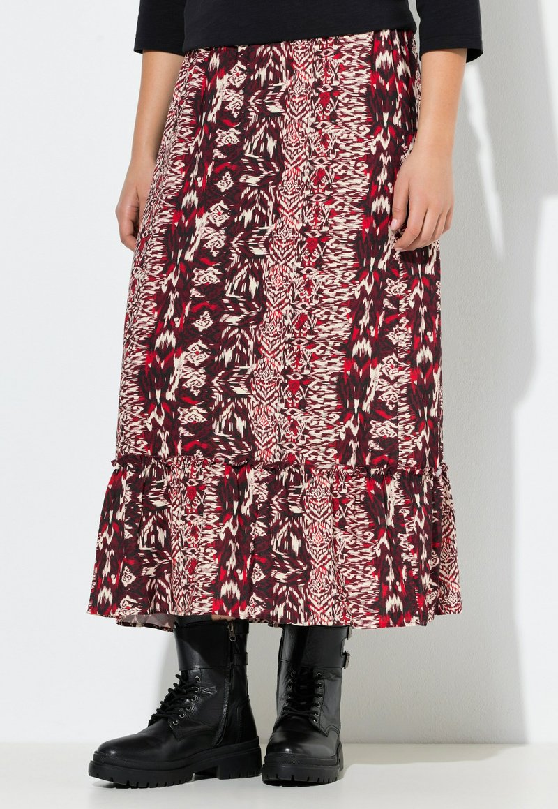 Mujer que lleva una falda midi con un estampado rojo y negro y un dobladillo con volantes, combinada con unas botas de combate negras con cordones y una blusa negra.