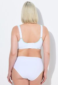 Sostén blanco con acentos en verde menta, tirantes ajustables y cierre de gancho y ojal. Combinado con pantalones de cintura alta blancos.