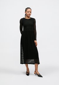 Black long-sleeve dress with a textured bodice and sheer, pleated skirt. Features a round neckline and a flowing silhouette.