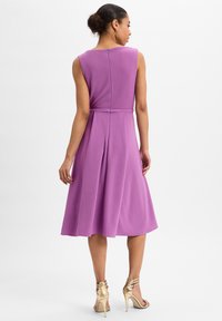 Lila ärmelloses Kleid mit tailliertem Schnitt, ausgestelltem Rock und Reißverschluss auf der Rückseite. Die Textur wirkt glatt mit einem leichten Glanz. Goldene Riemchenabsätze.