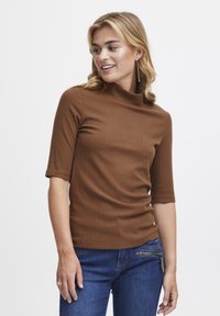 Brown, ribbed turtleneck top with short sleeves, fitted design, and smooth texture, paired with dark blue jeans featuring a zippered pocket.