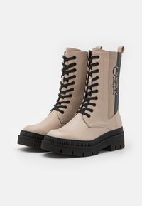 Boots de glezna din piele bej cu sireturi negre, talpă din cauciuc și detalii embossate "GMK" pe lateral. Prezintă un design drept și înalt.