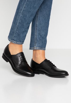 Sorte læder dress sko med en glat overflade, rund tå og snørebåndsdesign. Parret brugt med opsmøgede blå jeans.