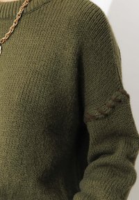 Pull en tricot vert olivine avec un col côtelé et des surpiqûres décoratives marron sur la manche. La texture douce améliore le confort.