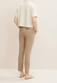 Pantalons beige slim-fit avec poches arrière, associés à un polo court en crème. Le tissu semble doux avec des manches courtes et un petit col.