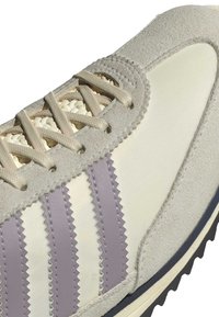 Light gray suede and cream fabric sneaker with zigzag purple stripes, flat beige laces, and textured rubber sole.