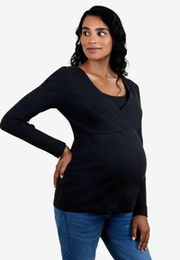 Schwarzes, geripptes Maternity-Top mit einem V-Ausschnitt, langen Ärmeln und einer taillierten Silhouette, kombiniert mit blauen Jeans.