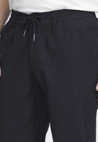 Navy blue linen pants with an elastic waist, drawstring closure, and side pockets. Smooth texture with a relaxed fit.