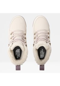 Botas de color beige claro con forro de pelo sintético, ojales de metal y cordones beige. Suela de goma plana y un logo en la plantilla negra. Con detalles en los tiradores de talón morados.