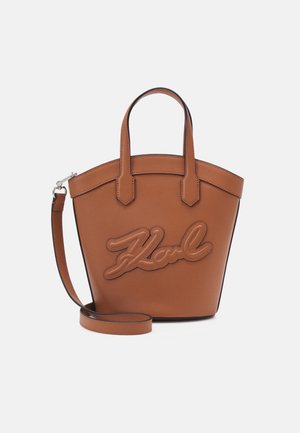 Braune Lederhandtasche mit zwei kurzen Griffen, einem abnehmbaren Schulterriemen und einem erhabenen Schriftzug auf der Vorderseite.