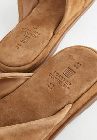 Chaussons en daim marron avec semelles intérieure rembourrées embossées du texte "Forever Comfort" et symbole en cuir, vue en gros plan.